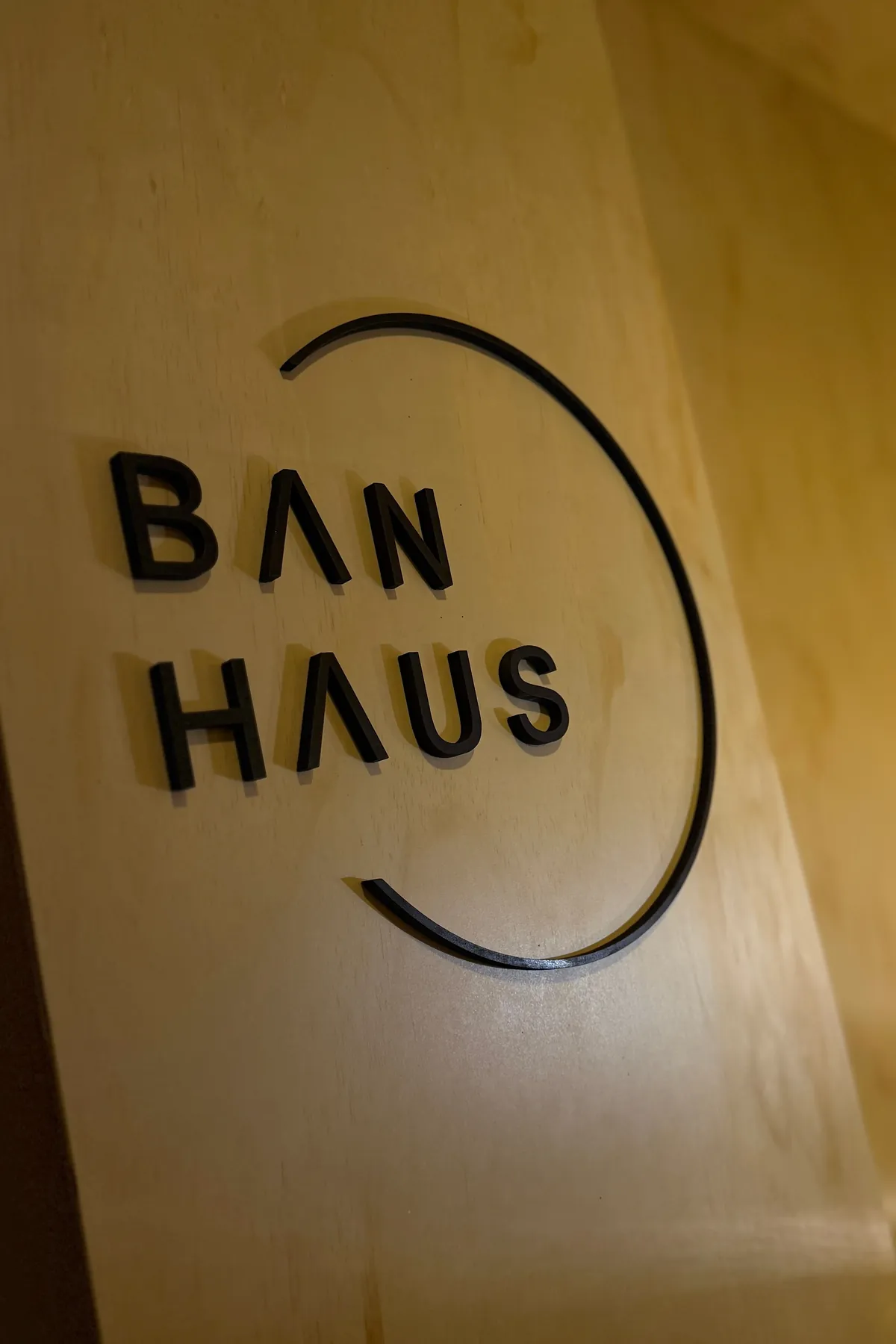 목재 판에 붙은 검은색 BAN HAUS 입체 사인과 열린 원형 선.